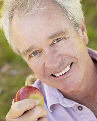 Adult man eating an apple with new immediate dentures in Boise
